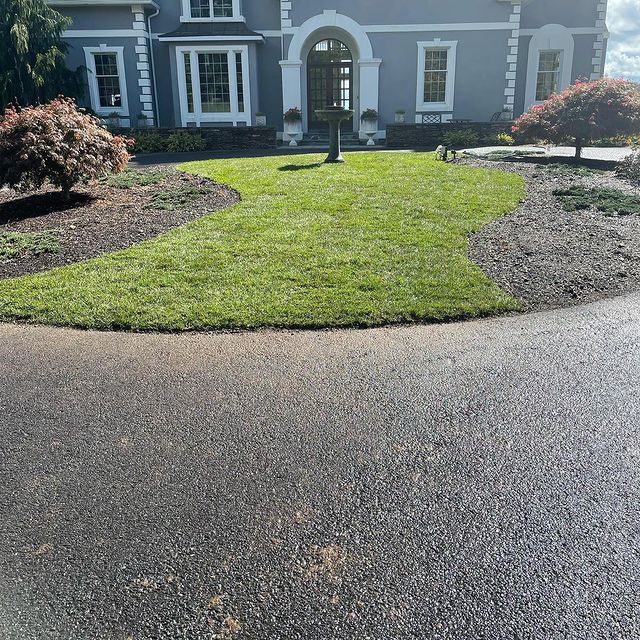 Landscaped area with two mulched areas with bushes and a birdfeeder center piece in front of a grey stucco home